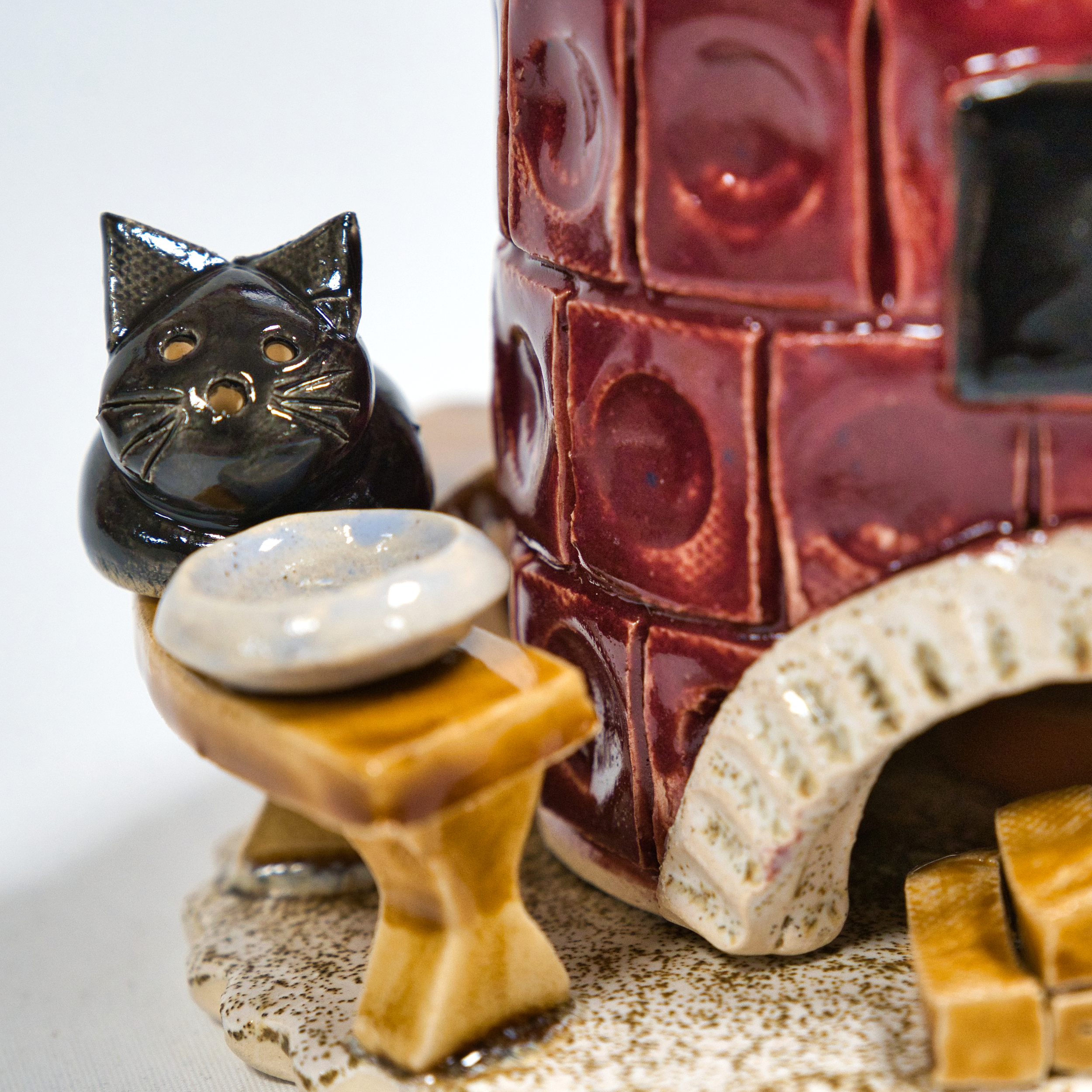 Eine handgefertigte Keramikskulptur zeigt eine schwarze Katze neben einer runden Schale neben dem Keramik-Räucherofen, Mini rund, altrosa von der Keramikwerkstatt Carola Busch. Dieser Keramikofen hat unten eine kleine Öffnung und steht auf einem wunderschön strukturierten Sockel.