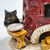 Eine handgefertigte Keramikskulptur zeigt eine schwarze Katze neben einer runden Schale neben dem Keramik-Räucherofen, Mini rund, altrosa von der Keramikwerkstatt Carola Busch. Dieser Keramikofen hat unten eine kleine Öffnung und steht auf einem wunderschön strukturierten Sockel.