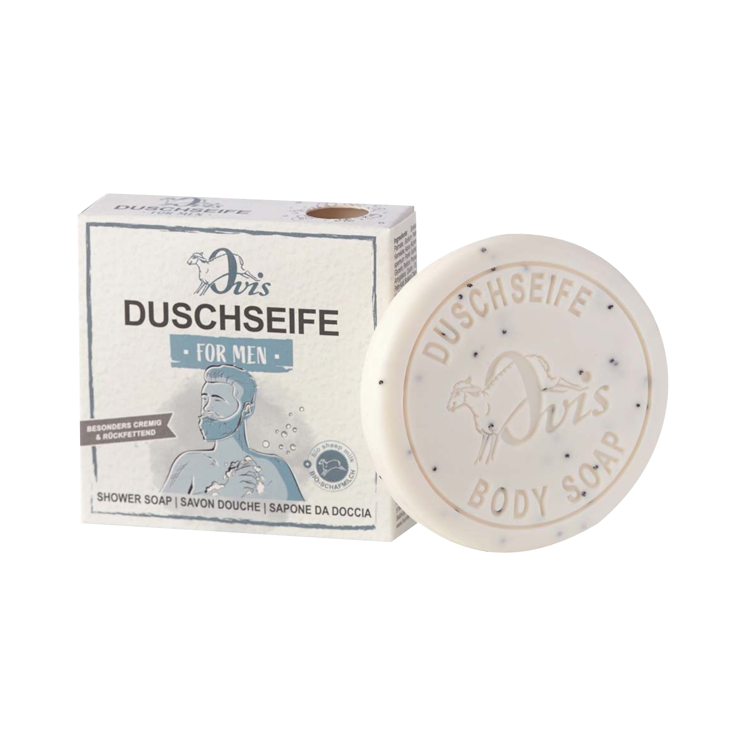 Ein runder Riegel Ovis Duschseife für Männer mit Sheabutter liegt neben der Schachtel, die einen bärtigen Mann beim Duschen zeigt und Text in Deutsch, Französisch, Italienisch und Englisch enthält.