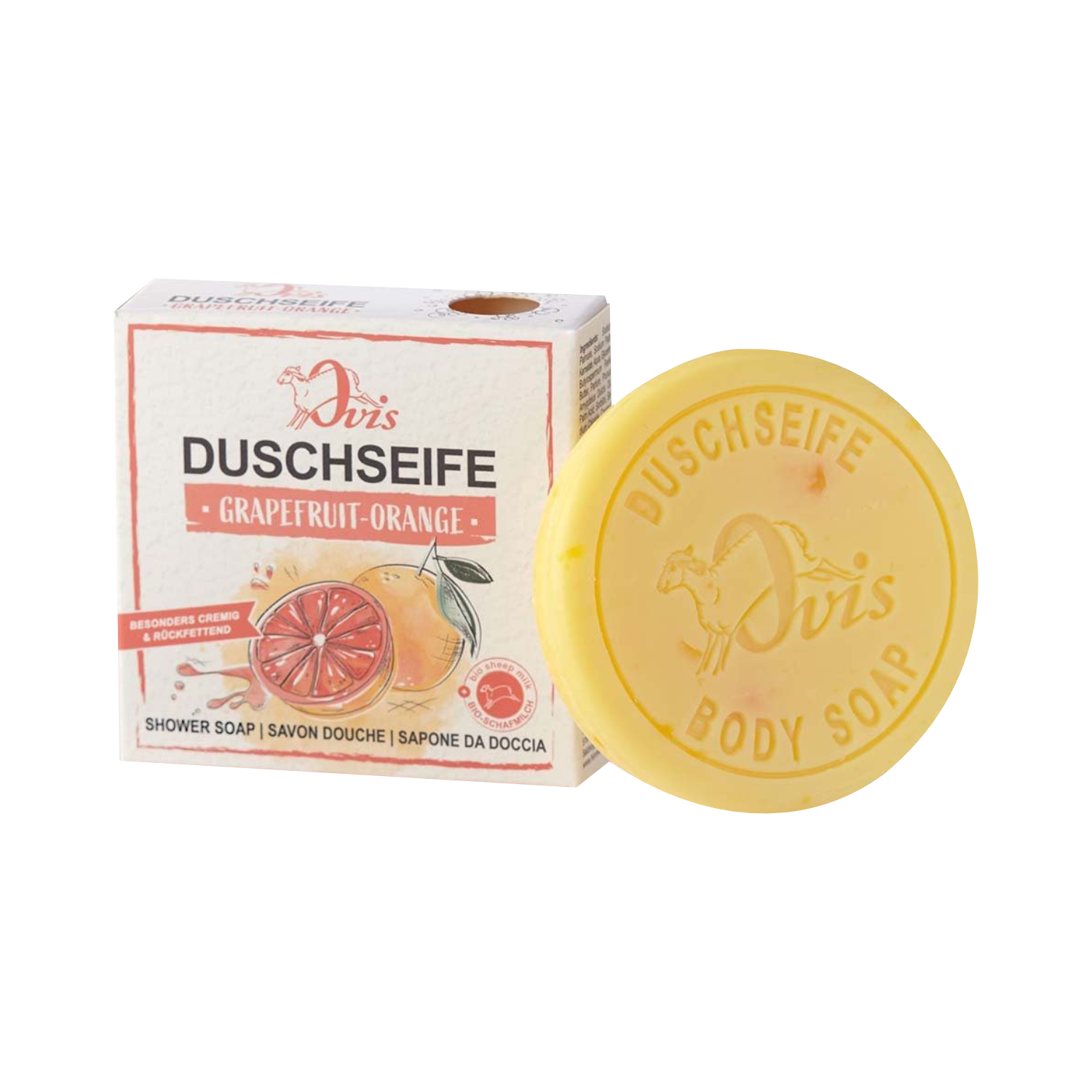Ein rundes gelbes Stück Ovis Duschseife Grapefruit-Orange liegt neben der Schachtel, die Bilder von Grapefruit und Orange zeigt und den Duft als Grapefruit-Orange kennzeichnet.