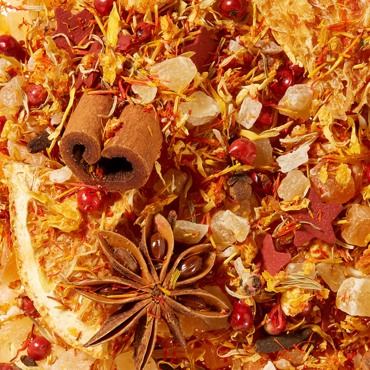 Eine Nahaufnahme von getrockneten Gewürzen und Früchten - Zimtstangen, Sternanis, Kandiszucker, Orangenscheiben, gelbe Blütenblätter - unterstreicht die lebendige Früchteteemischung