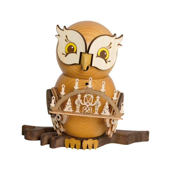 Die Rauchfigur Eule mit Schwibbogen von Drechslerei Kuhnert ist eine Holzeule mit großen Augen, die aus hellem und dunklem Holz gefertigt ist. Die Eule hält eine geschnitzte Brücke, die mit Räucherkerzen und Bäumen geschmückt ist und auf einem Ast thront.