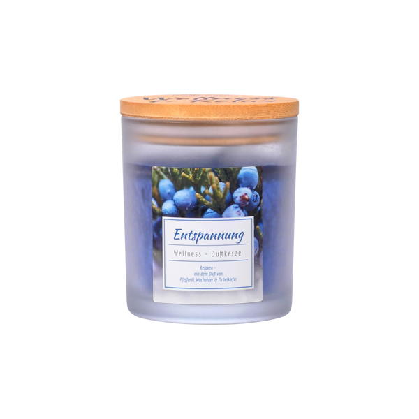 Die Candle Factory Wellness-Duftkerze "Entspannung" ist eine Stearinkerze aus Milchglas mit einem Holzdeckel. Auf dem mit Blaubeeren und Grünzeug verzierten Etikett stehen Duftnoten in deutscher Sprache und der Name "Entspannung".