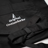 Crottendorfer Räucherkerzen-Schürze schwarz, gefaltet, mit Detailansicht vom Logo und Schleife
