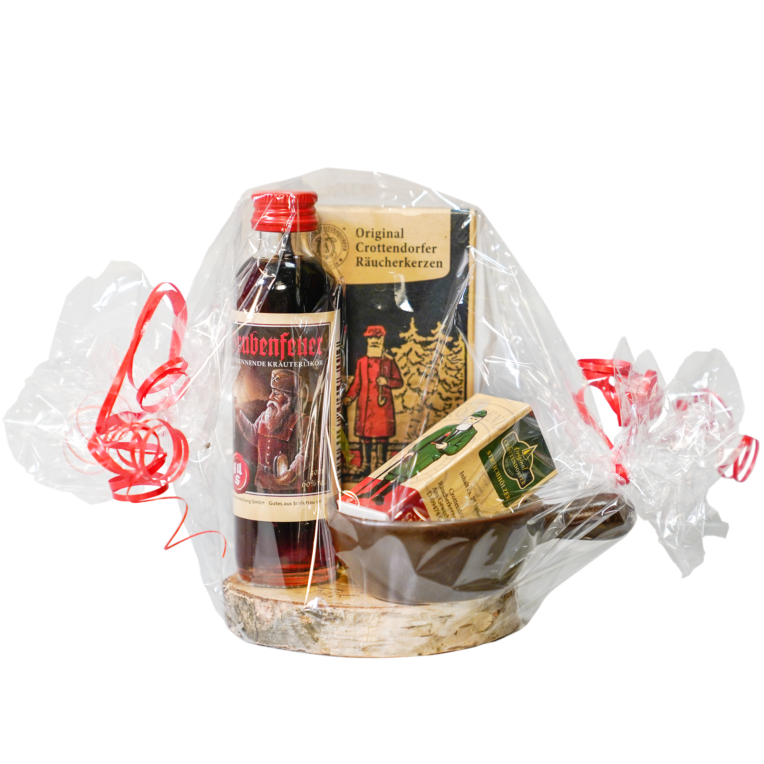 Das Geschenkset Grubenfeuer von Original Crottendorfer ist in transparenter Zellophanfolie mit roter Schleife verpackt und beinhaltet Kräuterbitter mit rotem Etikett, eine festliche Schachtel mit Weihnachtsbaum- und Weihnachtsmannmotiven, eine rechteckige Schachtel und eine flache braune Schale auf rundem Holzsockel. Ideal für Traditionsliebhaber.