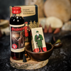 Auf einem Holztablett wird das Geschenkset Grubenfeuer präsentiert, das eine Original Crottendorfer Kräuterbitterflasche mit einer bärtigen Figur, eine Räucherkerzenschachtel mit Soldatenmotiv und eine kleine Räucherkerze enthält, alles reizvoll ergänzt durch einen braunen becherartigen Halter darunter.