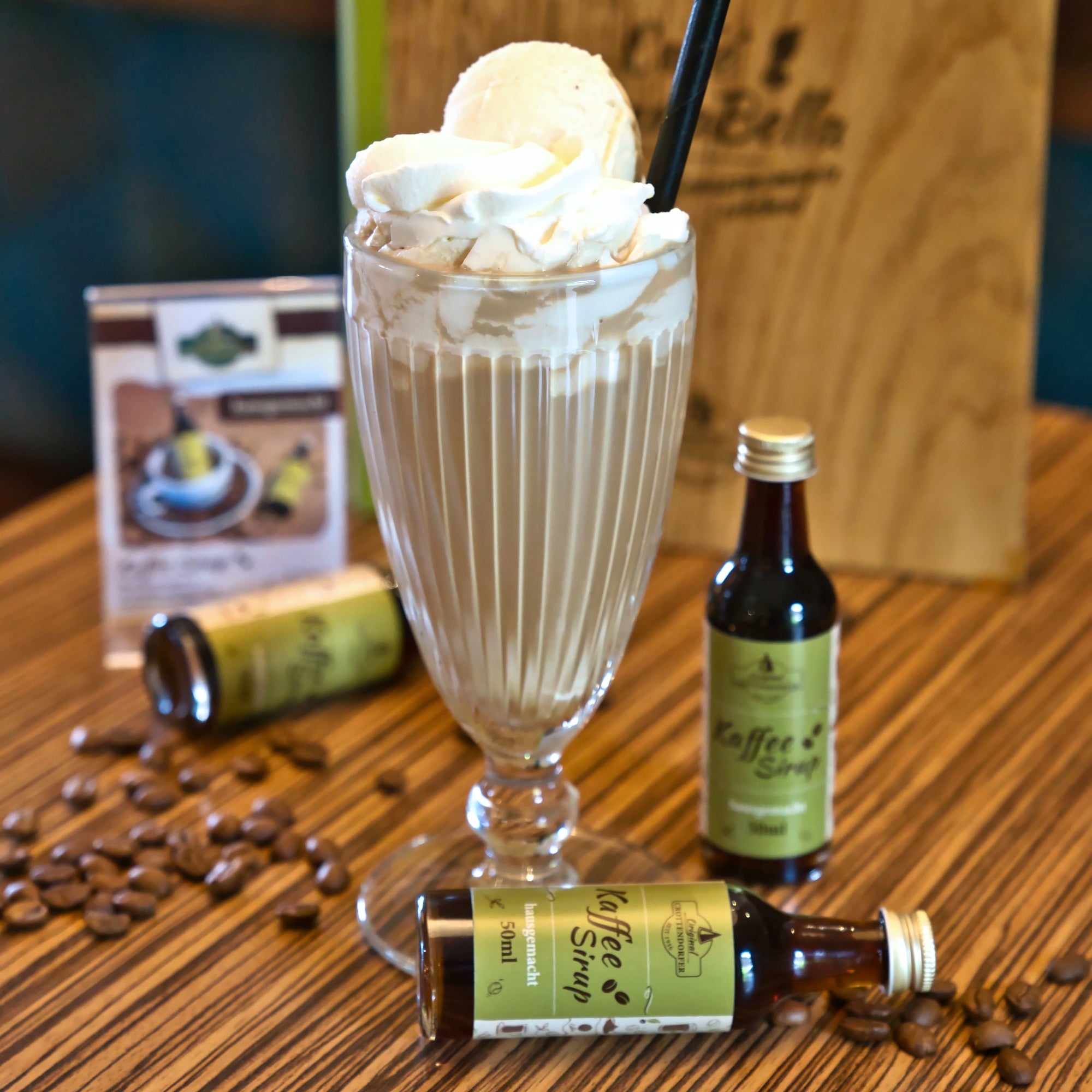 Ein großes Glas Eiskaffee mit Schlagsahne und Vanilleeis, dazu 50 ml Hausgemachter Kaffeesirup von Original Crottendorfer und Kaffeebohnen – ein perfekter Genuss für Kaffee- und Dessertliebhaber.