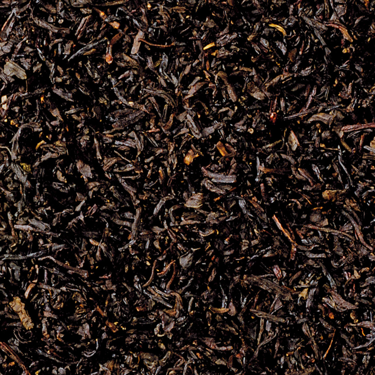 Eine Nahaufnahme des Schwarztees „Raacherkerzl-Tee“ von Original Crottendorfer zeigt lose schwarze Teeblätter mit einer satten, dunklen Farbe und einer gekräuselten, getrockneten Textur, die mit ihrem Hauch von Bergamotte-Essenz ein dichtes Aussehen ähnlich dem klassischen Earl Grey erzeugt.