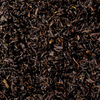 Eine Nahaufnahme des Schwarztees „Raacherkerzl-Tee“ von Original Crottendorfer zeigt lose schwarze Teeblätter mit einer satten, dunklen Farbe und einer gekräuselten, getrockneten Textur, die mit ihrem Hauch von Bergamotte-Essenz ein dichtes Aussehen ähnlich dem klassischen Earl Grey erzeugt.