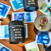 Mehrere schwarze Blechdosen von Original Crottendorfer Räucherkerzen, beschriftet mit "Räucherfass runder Geburtstag", liegen auf einem Holztisch mit buntem Spielgeld. Eine geöffnete Dose zeigt einen Münzschlitz und ein Wachssiegel - perfekt für das Räuchervergnügen unterwegs.