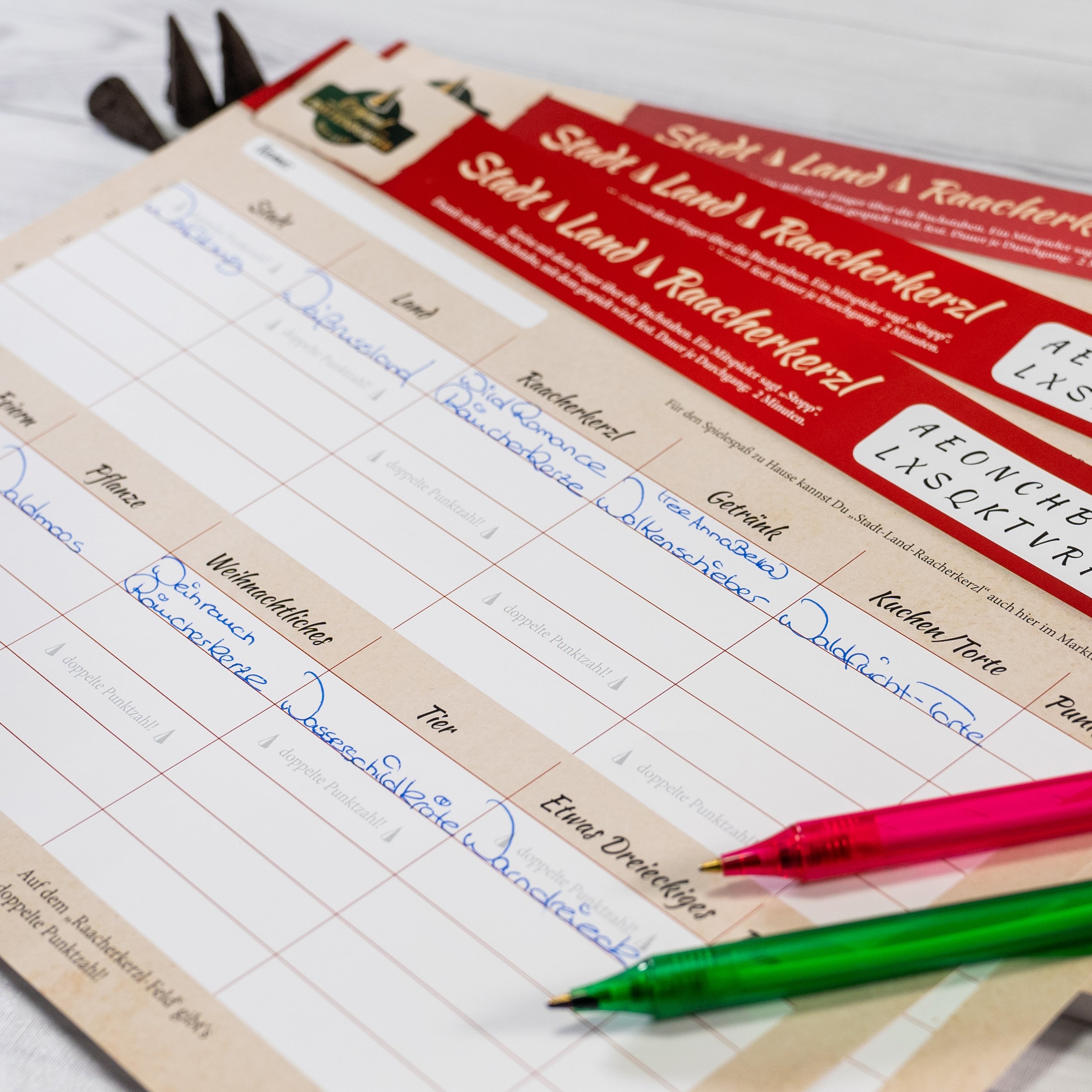 Die Nahaufnahme eines deutschen Dokuments offenbart kreatives Denken mit handgeschriebenem Text in blauer Tinte, roten und beigen Abschnitten sowie gedruckten Überschriften. Zwei Stifte, einer rot und einer grün, liegen auf dem Papier und erinnern an Original Crottendorfers Familienspaß „Stadt-Land-Raacherkerzl“ inmitten teilweise sichtbarer Werkzeuge.
