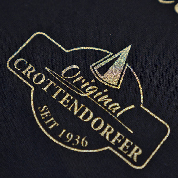 Goldtext und ein geometrisches Design auf Schwarz lauten: Stoffbeutel „Raacherkerzl Definition“ oder „Bitte nicht schubsen ...“ von Original Crottendorfer und spiegeln das erzgebirgische Erbe der Marke wider.