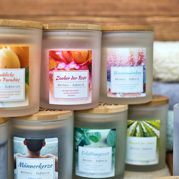 In einer gemütlichen Auslage steht die Candle Factory Wellness-Duftkerze Zauber der Rose, eine mattierte Glasduftkerze mit Holzdeckel, farbenfrohem Etikett und sanftem Stearin-Glühen - perfekt, um jedem Raum Wärme zu verleihen.