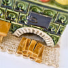 Nahaufnahme der Miniatur „Keramik-Küchenherd Zuckerbäckerei grün, eckig“ von der Keramikwerkstatt Carola Busch, die einem alten Kachelofen mit grünen Kacheln, einer schwarzen Tür und Holzscheiten unter einem weißen Bogen ähnelt. Er ruht auf einer leicht strukturierten Oberfläche.