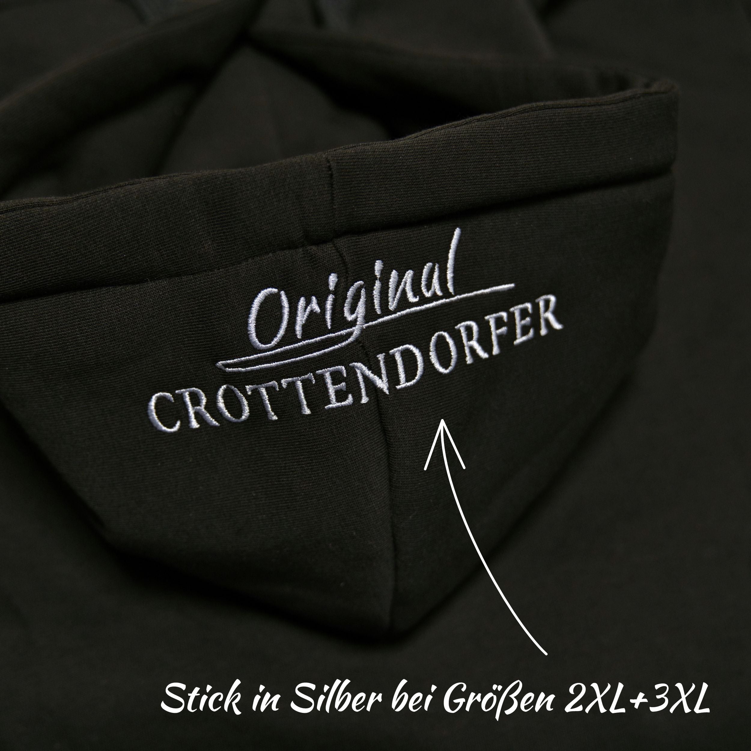 Nahaufnahme des Kapuzenpullovers „Crottendorfer Räucherkerzen“ von Original Crottendorfer in Schwarz mit weiß gesticktem „Original CROTTENDORFER“-Schriftzug. Silberner Stick für die Größen 2XL & 3XL; der Pfeil zeigt auf die klassische Stickerei im Streetwear-Stil.