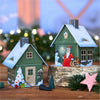 Zwei metallene Räucherhäuschen Weihnachten von Original Crottendorfer Räucherkerzen stehen auf einer Holzfläche und sind mit festlichen Motiven von Weihnachtsmann, Schneemann und Weihnachtsbaum geschmückt. Schneebedeckte Dächer und verschwommene Lichter unterstreichen das Weihnachtsthema und sorgen für bezaubernde Dekorationen.