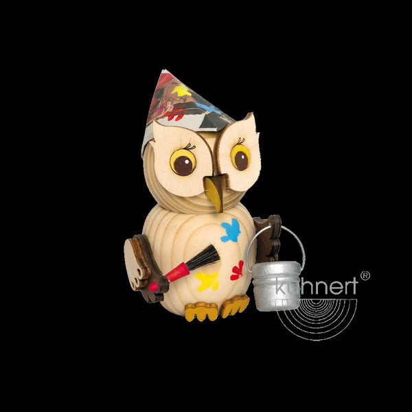Der Mini Eule Maler der Drechslerei Kuhnert aus nachhaltig gewonnenem Holz hat einen bunt bemalten Papierhut. Er hält einen Pinsel und einen Metalleimer, hat helle Farbspritzer und große runde Augen auf schwarzem Hintergrund.