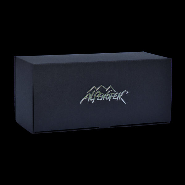Eine schwarze rechteckige Schachtel mit einem Logo mit Berggipfeln und „Alpenofen“ in Silber, das die exquisite Handarbeitstradition aus dem Erzgebirge zur Schau stellt und die Qualität von „Alpenofen eckig“ widerspiegelt.