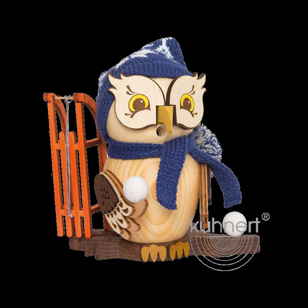Die „Rauchfigur Eule mit Schlitten“ von Drechslerei Kuhnert zeigt eine bezaubernde Holzeule mit blauer Strickmütze und Schal, die einen weißen Schneeball neben einem orangefarbenen Schlitten hält und so den unverwechselbaren Rauchfiguren-Stil einfängt. Auf dem Sockel ist der Markenname „Kuhnert“ abgebildet.