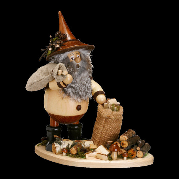 Die Figur „Uhlig Waldwichtel Astsammler“ der DWU Drechselwerkstatt verströmt mit ihrem Holzbart, dem hexenähnlichen Hut, den orangefarbenen Stiefeln und der kleinen Tasche, umgeben von Holzscheiten und Pilzen auf einem runden Sockel, einen skurrilen, rustikalen Charme und verkörpert den Volkskunstgeist des Original Erzgebirges.