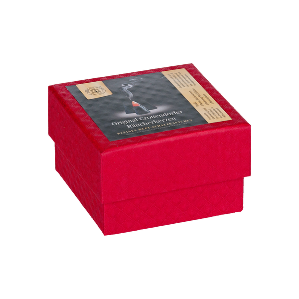 Die Geschenkbox „Wunschduft“ von Original Crottendorfer Räucherkerzen ist eine rote, quadratische Schachtel mit einem Deckel, auf dem ein Etikett mit dem Bild eines rauchenden Räuchergefäßes abgebildet ist, das an traditionelle Räucherkerzen-Rituale erinnert.