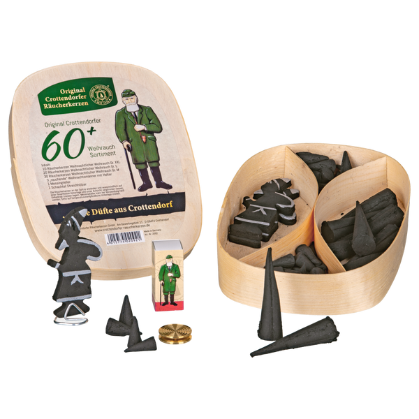 Das Geschenkset Spanschachtel 60+ von Original Crottendorfer Räucherkerzen besteht aus einer Holzkiste mit schwarzen Räucherkegeln, dekorativen Räucherformen, einer Streichholzschachtel mit einer Figur und einem Holzdeckel mit deutschem Text.