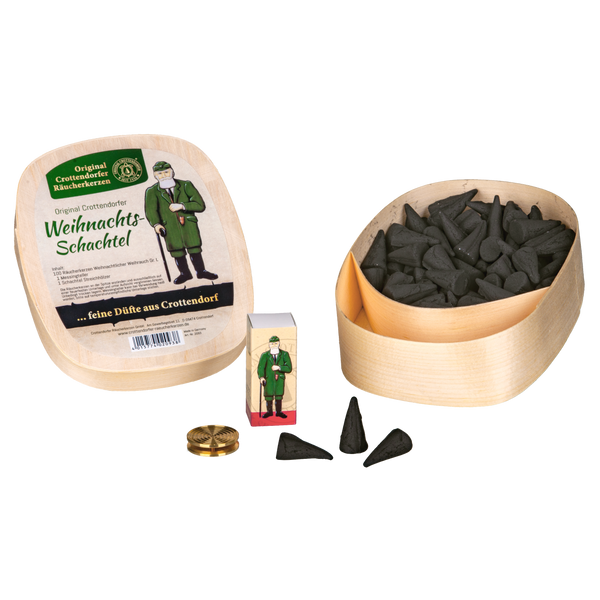 Das Geschenkset Weihnachts-Schachtel von Original Crottendorfer Räucherkerzen enthält eine Holzkiste mit schwarzen Räucherkegeln, eine Streichholzschachtel mit einem Mann, einen Messingtellerhalter aus Messing und mehrere Räucherkegel, die auf einer weißen Fläche angeordnet sind.
