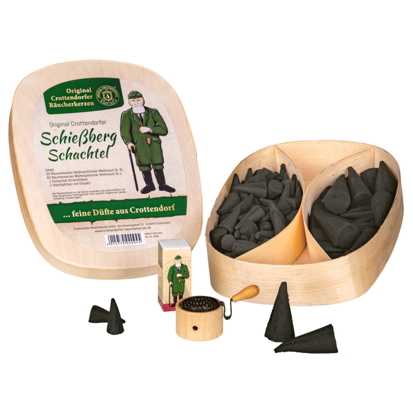 Das Geschenkset 'Schießberg'-Schachtel von Original Crottendorfer Räucherkerzen enthält eine Holzbox, kleine schwarze Weihrauchkegel, eine Mini-Räucherfigur aus Holz und eine kleine runde Reibe, wobei einige Kegel außerhalb der Box ausgestellt sind.