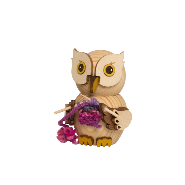 Die MINI Eule mit Strickzeug von Drechslerei Kuhnert ist eine exquisite Figur, die Stricknadeln mit lila Garn hält. Ihre geschnitzten Gesichtszüge und Flügel unterstreichen die feine Handwerkskunst, während das verspielte Garn von den Nadeln baumelt.
