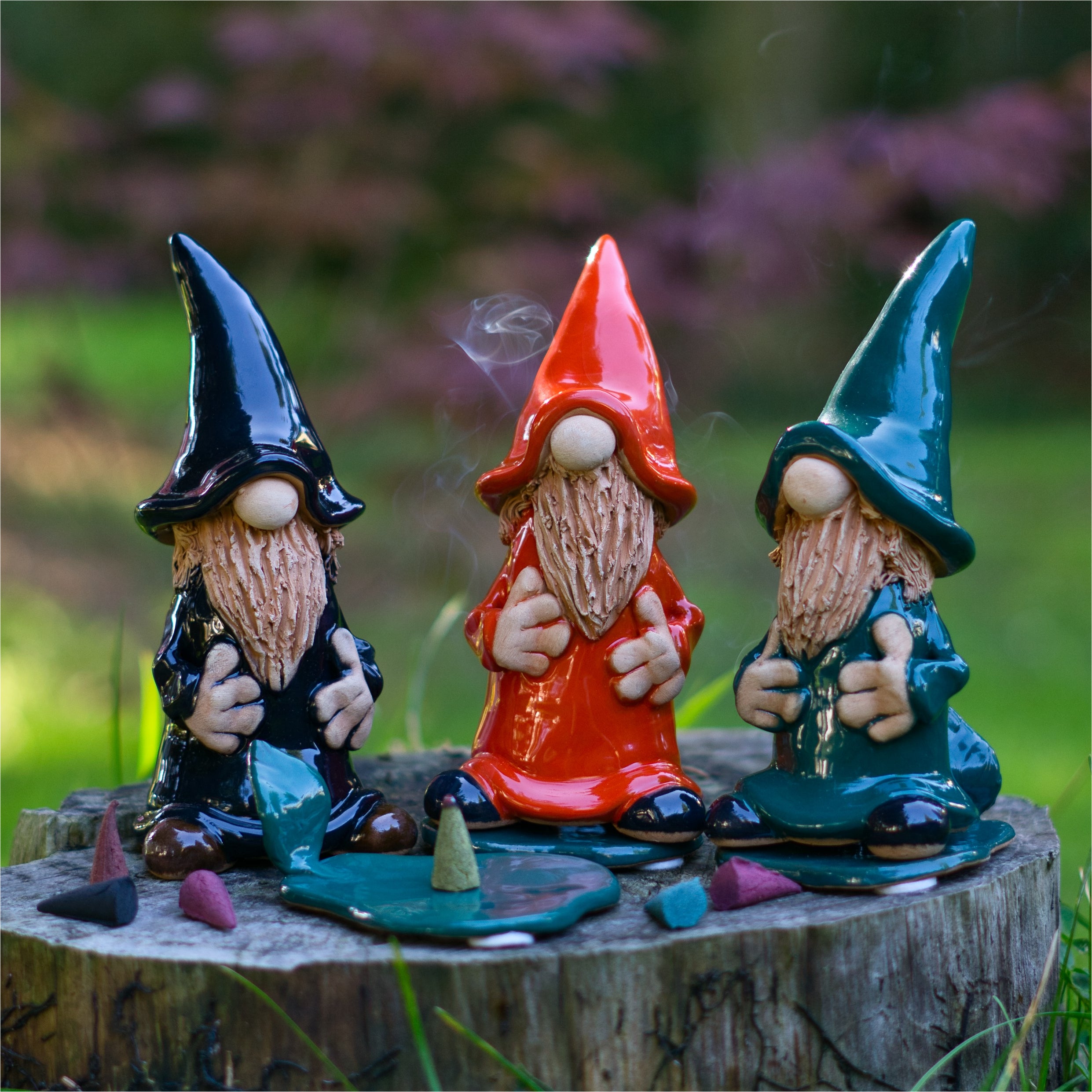 Die Keramik-Räucherfigur Wichtel - schwarz von Original Crottendorfer Räucherkerzen sitzt auf einem Baumstumpf, umgeben von bunten Räucherkerzen; Rauch steigt auf. Leichte Abweichungen in Design und Farbe sind möglich.