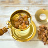 Auf einer hellen Holzoberfläche steht ein goldenes Räuchergefäß mit Holzgriff, gefüllt mit Räucherharz Myrrhe 20g von Original Crottendorfer Räucherkerzen. Zusätzliche Myrrhe- und Räucherstoffe sind in der Nähe verstreut, ideal für die Schaffung einer Schutz- und Reinigungsweihrauch-Atmosphäre.