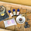 Ein Plantaroma-Holztablett bietet ein Aromatherapie-Set mit einem Ölbrenner aus Glas, drei ätherischen Ölflaschen, Räuchersand in einem Beutel und einer weißen Schale mit Quarzsand und einer mit Kräutern belegten Kohlescheibe. Für ein noch intensiveres Erlebnis sind zusätzliche Kohlescheiben und eine Zange im Lieferumfang enthalten.