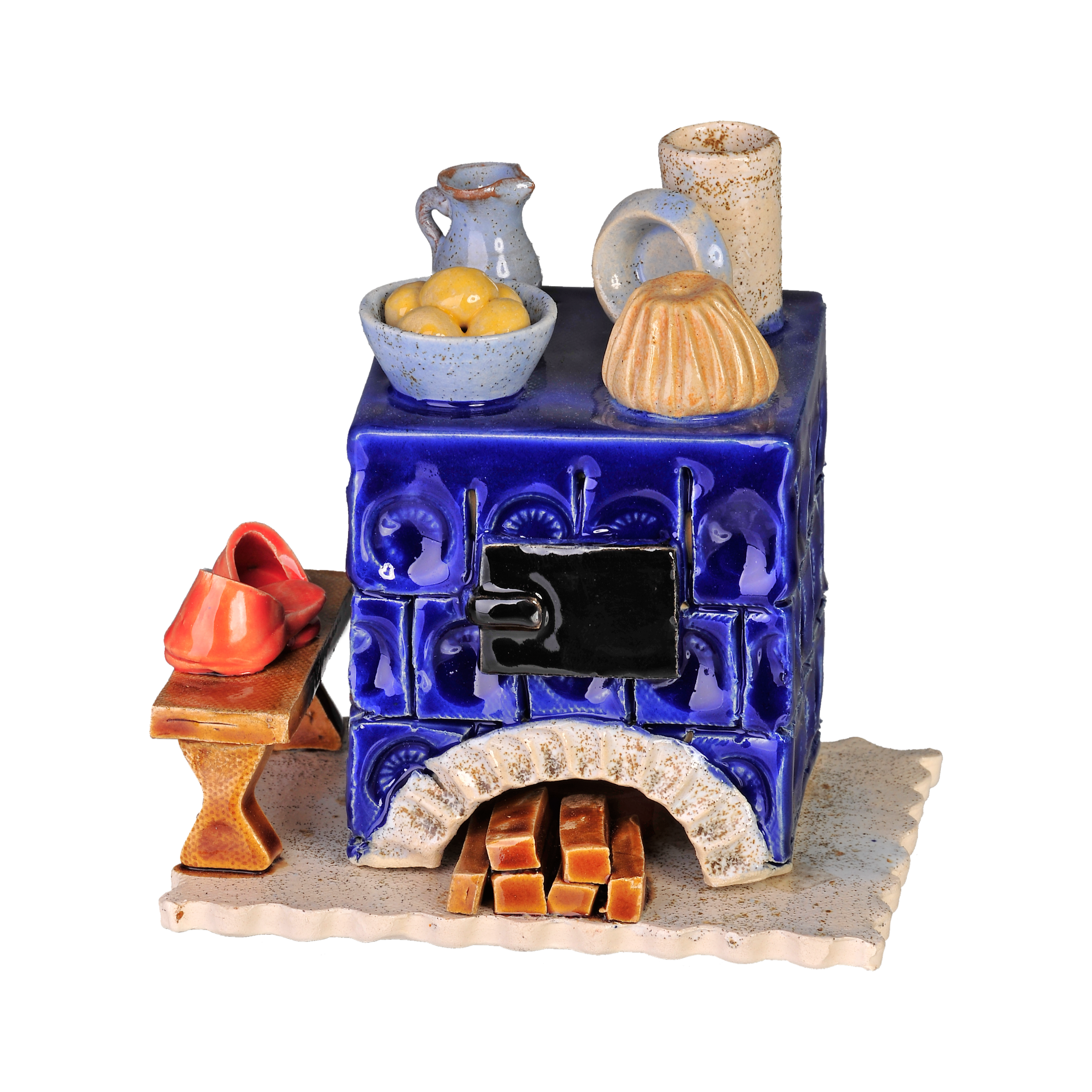 Der Keramik-Räucherofen Mini eckig, blau von der Keramikwerkstatt Carola Busch ist ein dekorativer blauer Keramikofen mit aufwendigen Mustern, auf dem sich eine Obstschale, ein Krug und ein Formkuchen befinden. Am Sockel ist handgefertigtes Brennholz gestapelt, daneben liegen rote Holzschuhe, die seinen charmanten Reiz unterstreichen.