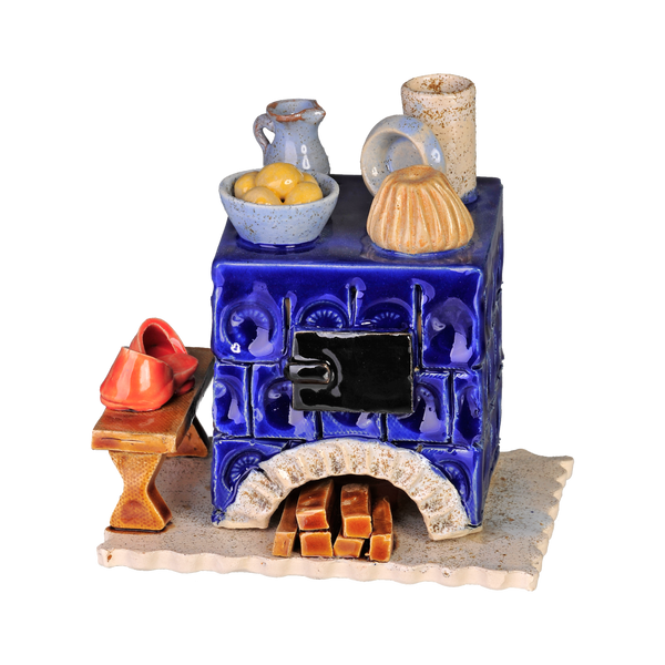 Der Keramik-Räucherofen Mini eckig, blau von der Keramikwerkstatt Carola Busch ist ein dekorativer blauer Keramikofen mit aufwendigen Mustern, auf dem sich eine Obstschale, ein Krug und ein Formkuchen befinden. Am Sockel ist handgefertigtes Brennholz gestapelt, daneben liegen rote Holzschuhe, die seinen charmanten Reiz unterstreichen.