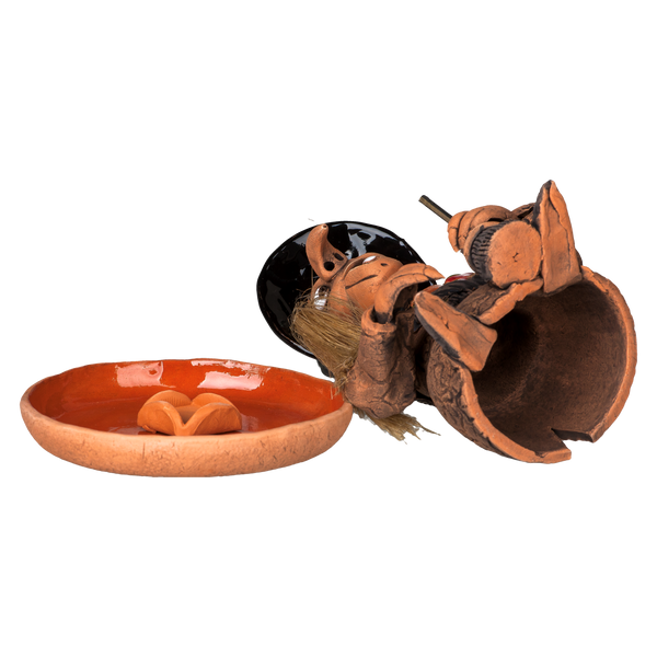 Eine zerbrochene „Räucherhexe mit Keramikteller - Hut schwarz“ von Original Crottendorfer, die einer Hexenfigur mit schwarzem Hut ähnelt, liegt neben einer orangefarbenen Schale mit Mini-Kürbissen. Dieses Unikat ist Teil unserer Limited Edition-Kollektion und in begrenzten Stückzahlen erhältlich.