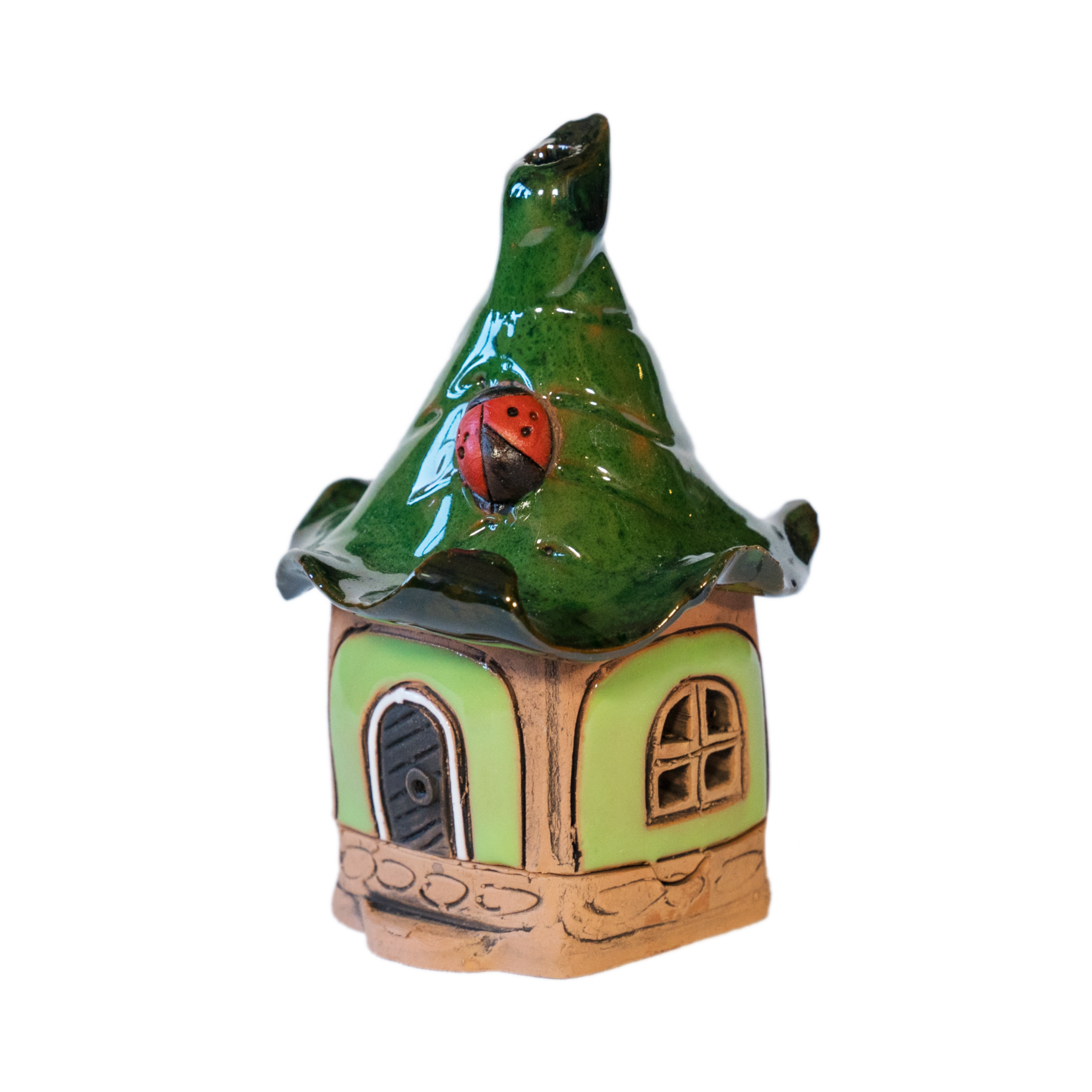 Das Original Crottendorfer Räucherhaus Keramik mini grün mit Marienkäfer hat ein skurriles Design mit einem grünen, gewellten Dach, auf dem ein rot-schwarzer Marienkäfer sitzt. Es hat eine blassgrüne Außenseite, eine Holztür, ein rundes Fenster und ruht auf einem Steinsockel für eine auffällige Präsentation.