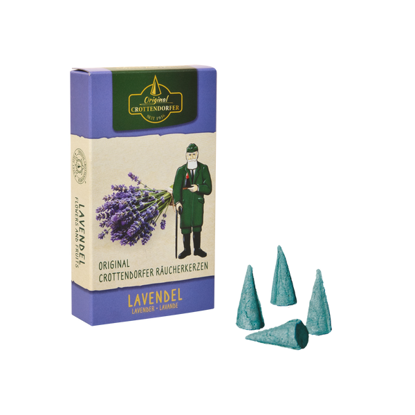 Eine Schachtel mit Original Crottendorfer Räucherkerzen „Lavendel“ ist neben vier blaugrünen Räucherkegeln abgebildet. Die Verpackung zeigt eine Illustration von Lavendel und einer grün gekleideten Person, die an den blumigen Duft der Provence erinnert.