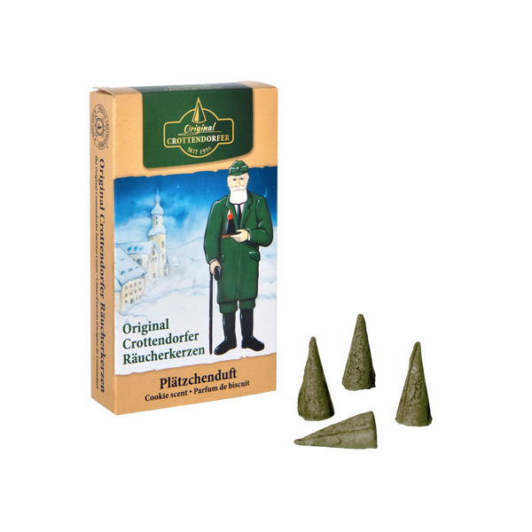 Auf der Verpackung einer Schachtel Original Crottendorfer Räucherkerzen „Räucherkerzen Plätzchenduft“ ist ein Mann in Grün mit einer Kirche abgebildet. Vier grüne Räucherkegel stehen bereit, um Ihren Raum mit ihrem herrlichen Butterkeksduft zu erfüllen.