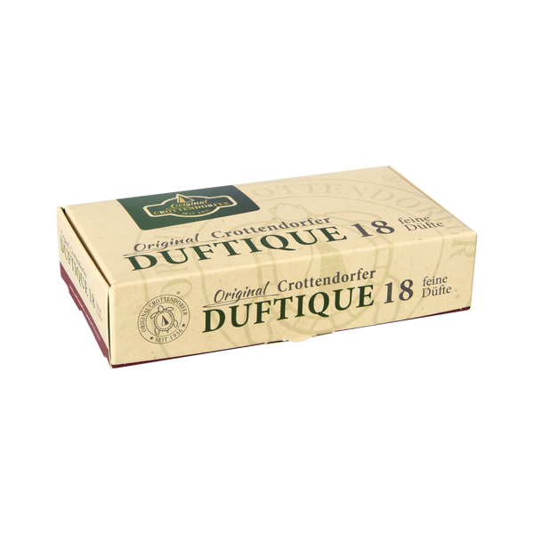 Rechteckige, beige Verpackung von „Original Crottendorfer DUFTIQUE 18 feine Düfte“ auf weißem Hintergrund. Die Schachtel zeigt oben ein grünes Logo mit der Aufschrift „Original CROTTENDORFER SEIT 1936“ sowie unten links ein runden Stempel mit einer Schildkröte und der Aufschrift „ORIGINAL CROTTENDORFER – SEIT 1936“. Auf der Schachtel steht der Text: „Original Crottendorfer DUFTIQUE 18 feine Düfte“.