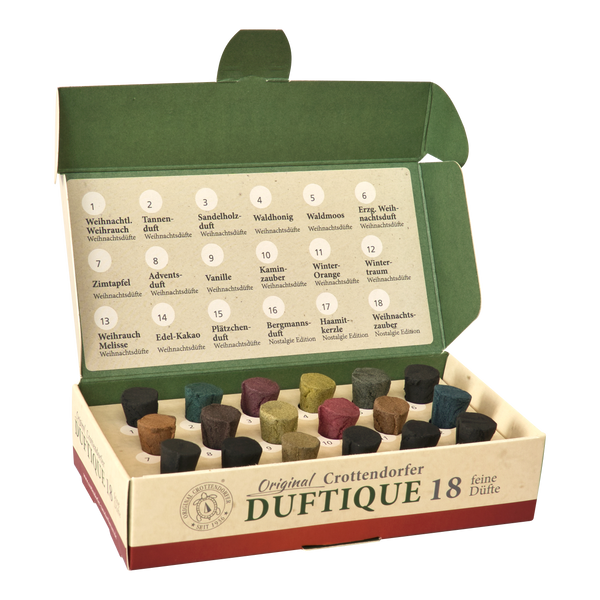 Geöffnete Schachtel mit Räucherkegeln „Duftique 18 feine Düfte – Weihnachtsdüfte & Editionen“ von Original Crottendorfer Räucherkerzen, in der sich 18 verschiedenfarbige Räucherkegel und eine gedruckte Liste der Düfte – wie Weihrauch, Tannenduft und andere festliche Sorten – in der beige-grünen, deutschsprachigen Schachtel befinden.