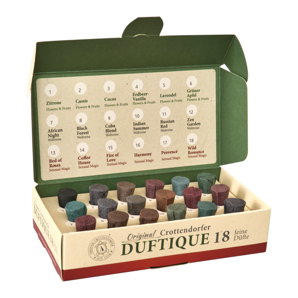 Eine geöffnete Schachtel mit der Aufschrift „Duftique 18 feine Düfte – Blumen & Früchte, Weltreise & Sinnliche Magie“ von Original Crottendorfer Räucherkerzen präsentiert 18 farbenfrohe Duftkegel in Reihen, die jeweils mit einem Duftnamen und einer Nummer auf der Innenseite des Deckels versehen sind und eine Weltreise durch blumige, fruchtige und holzige Düfte für eine exquisite Duftauswahl bieten.