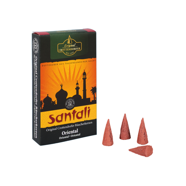 Eine Schachtel mit Original Crottendorfer Räucherkerzen Oriental – Räucherkegel, auf denen die Silhouette einer Moschee vor einem orangefarbenen Sonnenuntergang abgebildet ist, davor sind vier Räucherkegel angeordnet.