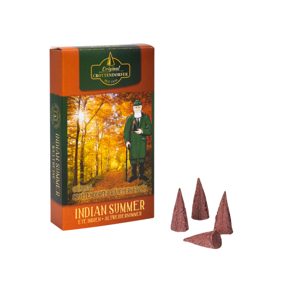 Abgebildet ist eine Schachtel „Räucherkerzen Indian Summer“ von Original Crottendorfer Räucherkerzen, die eine herbstlich gefärbte Waldszene mit einem Mann in traditioneller Kleidung zeigt. Vor der Schachtel sind vier braune Zapfen mit Karamellnoten platziert.