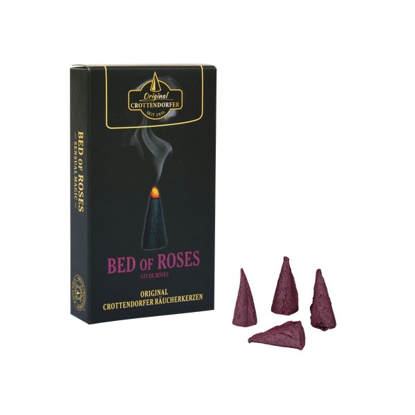 Eine Schachtel mit der Aufschrift „Räucherkerzen Bed of Roses“ von Original Crottendorfer Räucherkerzen steht aufrecht neben vier violetten Räucherkegeln vor einem weißen Hintergrund. Auf der Verpackung ist ein einzelner brennender Räucherkegel zu sehen, aus dem Rauch aufsteigt, was den zarten Duft von Rosen, vermischt mit einem Hauch von Moschus, heraufbeschwört.