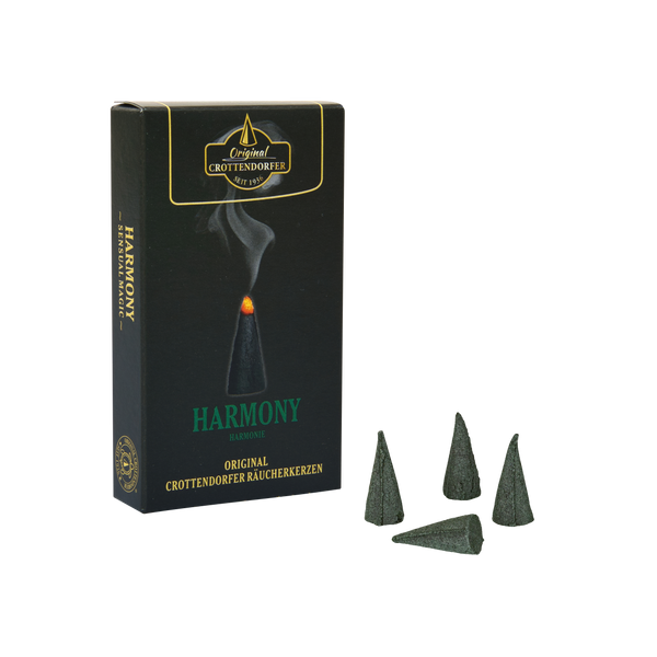 Eine schwarze Schachtel mit der Aufschrift „Räucherkerzen Harmony“ von Original Crottendorfer Räucherkerzen steht aufrecht neben vier grünen Räucherkegeln vor einem weißen Hintergrund und verströmt einen holzig-rauchigen, herbstlichen Duft – perfekt für gemütliche Herbstabende.