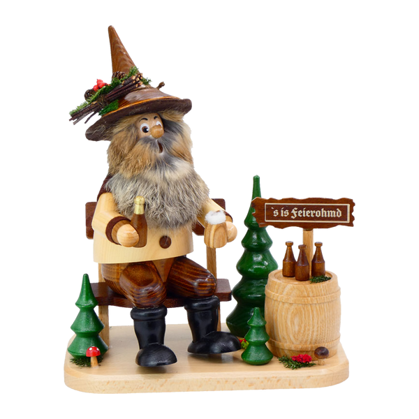 Die Waldwichtel Feierabend auf Bank von DWU Drechselwerkstatt Uhlig ist eine charmante erzgebirgische Holzfigur eines bärtigen Mannes mit Hut auf einer Bank mit einer Bierflasche, Bäumen, einem Fass mit Flaschen und einem "s is Feierohmd" Schild.