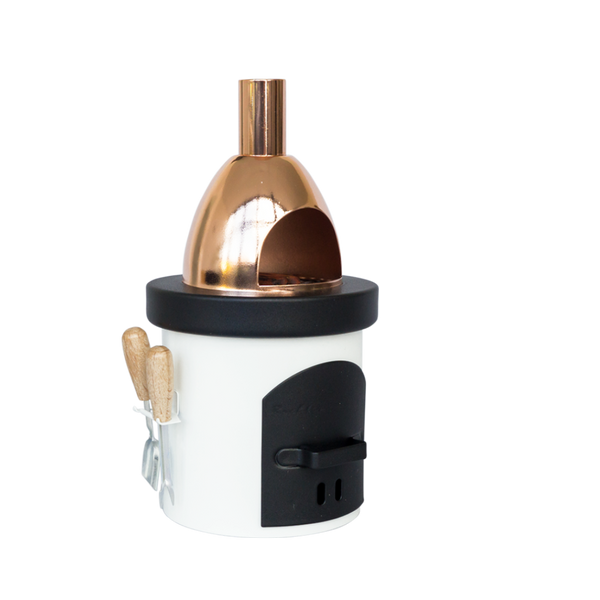 Der Räucherofen Grillofen von Hartmut Richter ist ein kompakter Tischpizzaofen mit glänzender Kupferkuppel, schwarzer Fronttür und weißem, zylindrischem Sockel, an dessen Seite zwei Utensilien mit Holzgriff hängen - alles vor einem schlichten weißen Hintergrund.
