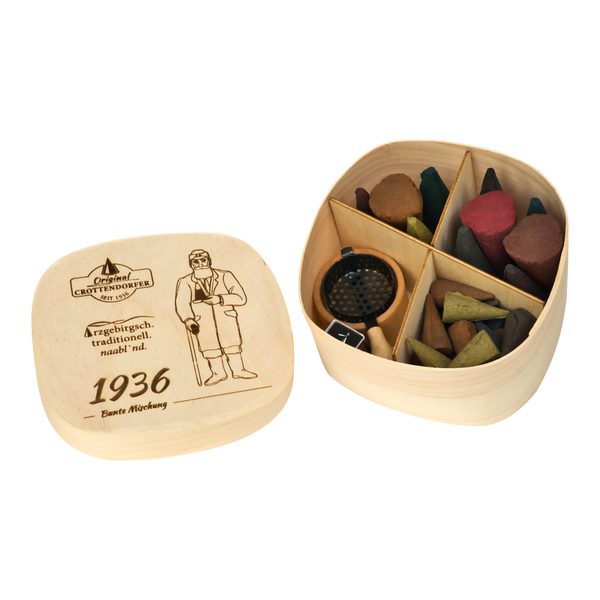 Die „Spanschachtel 1936“ von Original Crottendorfer Räucherkerzen ist eine Holzschachtel mit Deckel, auf der ein Mann und die Jahreszahl 1936 eingraviert sind. Sie ist mit bunten Räucherkegeln sowie einem unterteilten Metallhalter gefüllt – und damit ein ideales Geschenkset mit Räucherzubehör.