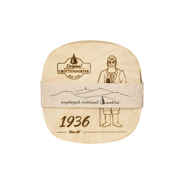 Die „Spanschachtel 1936“ von Original Crottendorfer Räucherkerzen ist eine Käsebox aus Holz, deren Vorderseite mit einer detailreichen Illustration eines Mannes in traditioneller Tracht, Bergsilhouetten und der Jahreszahl 1936 verziert ist, ergänzt durch deutsche Sprüche, die die Tradition des Erzgebirges würdigen. Diese bezaubernde Schachtel eignet sich ideal als Räucherzubehör oder als Teil eines unverwechselbaren Geschenksets.