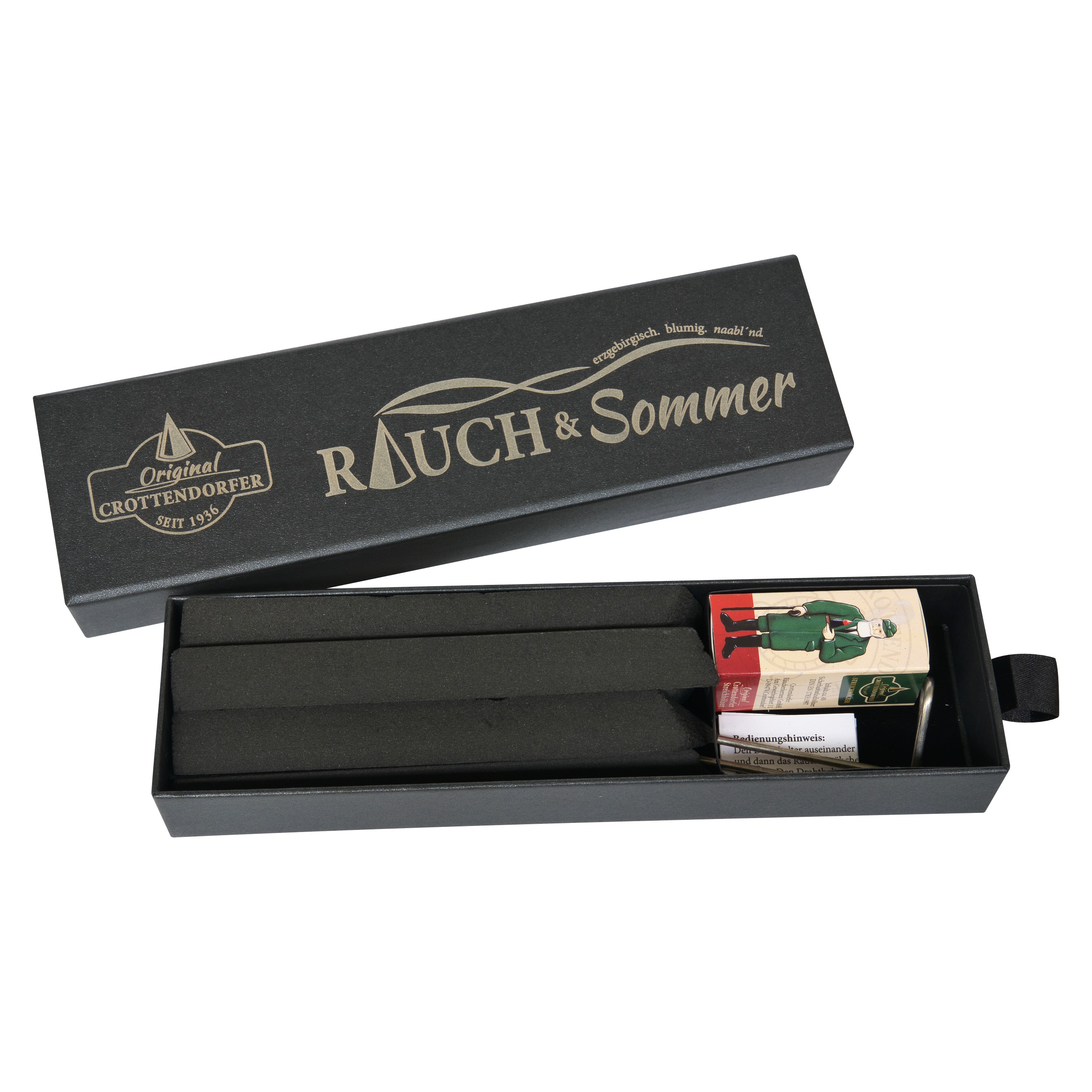 Eine offene, schwarze, rechteckige Schubbox von RAUCH & Sommer aus dem Sortiment von Original Crottendorfer Räucherkerzen enthält zwei lange schwarze Stäbchen und eine kleine Streichholzschachtel, auf der eine Person in grüner Kleidung abgebildet ist.
